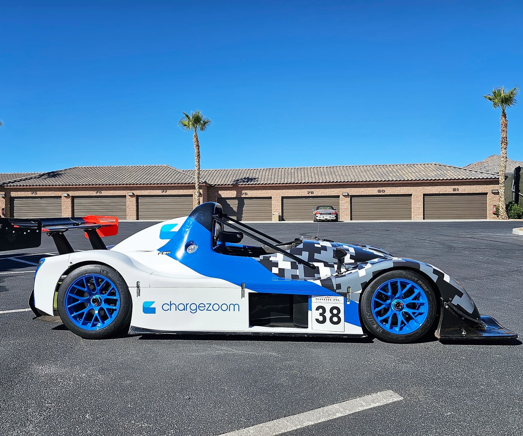 Blue and white number 38 Radical race car with chargezoom livery parked in a desert paddock