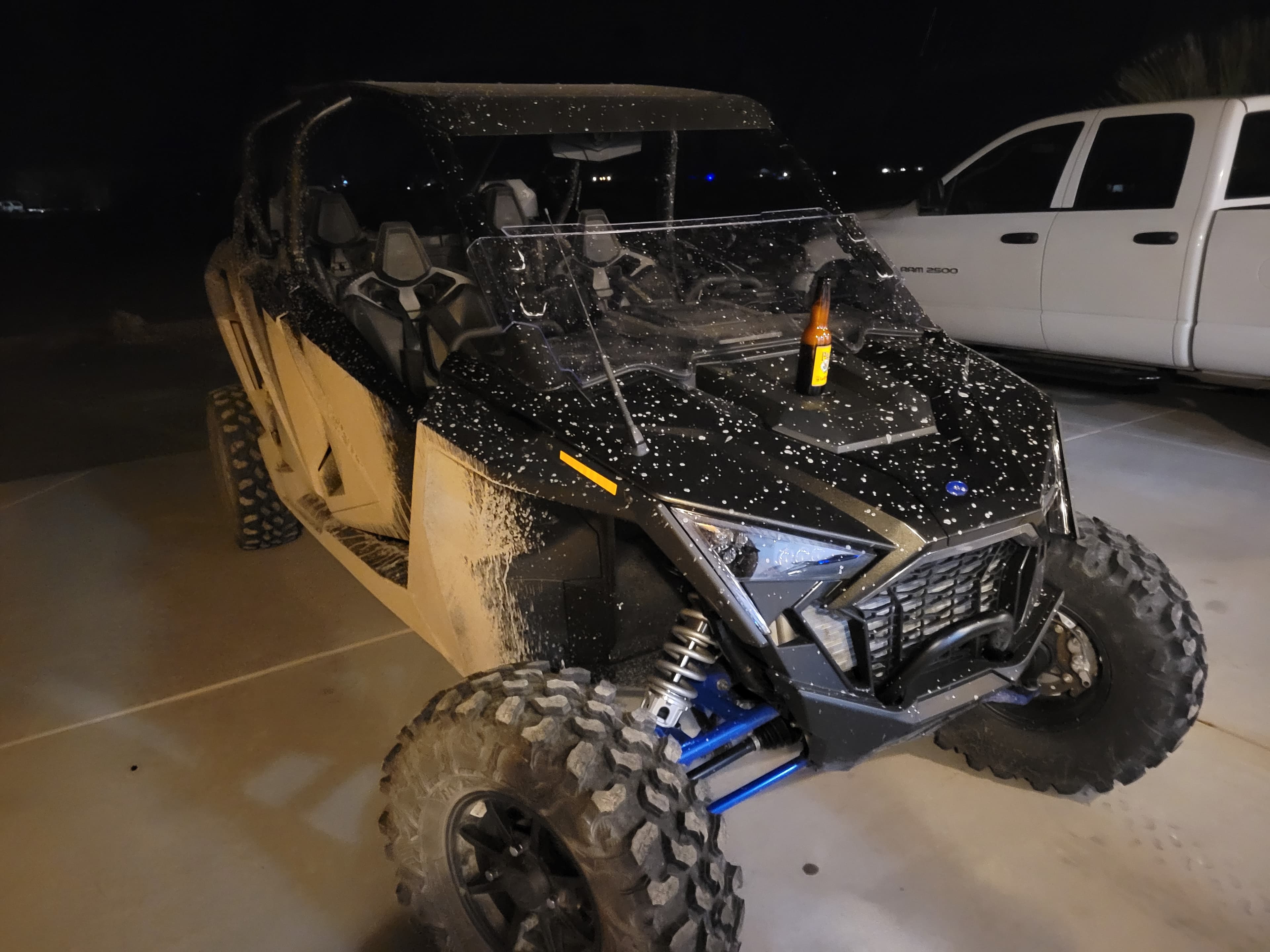 Black Polaris RZR side-by-side caked in dried mud splatter parked at night beside a pickup truck